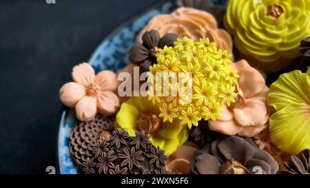 Thailändisches Dessert in verschiedenen blumenförmigen, warmen Farbtönen, Orangen-, Schokoladen- und Mangoaroma, Sam Pan Nee traditioneller thailändischer Snack in dunklem Hintergrund Stockfoto