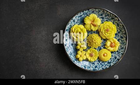 Thailändisches Dessert in verschiedenen blumenförmigen, warmen Farbtönen, gelber Mangogeschmack auf antikem Muster, Sam Pan Nee traditioneller thailändischer Snack in Stockfoto