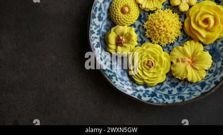 Thailändisches Dessert in verschiedenen blumenförmigen, warmen Farbtönen, gelber Mangogeschmack auf antikem Muster, Sam Pan Nee traditioneller thailändischer Snack in Stockfoto