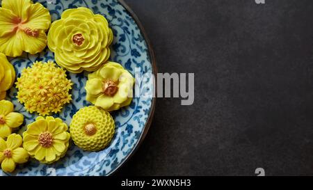 Thailändisches Dessert in verschiedenen blumenförmigen, warmen Farbtönen, gelber Mangogeschmack auf antikem Muster, Sam Pan Nee traditioneller thailändischer Snack in Stockfoto