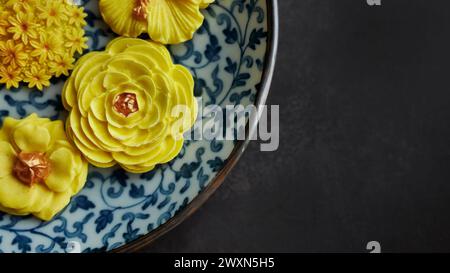 Thailändisches Dessert in verschiedenen blumenförmigen, warmen Farbtönen, gelber Mangogeschmack auf antikem Muster, Sam Pan Nee traditioneller thailändischer Snack in Stockfoto