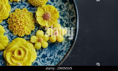 Thailändisches Dessert in verschiedenen blumenförmigen, warmen Farbtönen, gelber Mangogeschmack auf antikem Muster, Sam Pan Nee traditioneller thailändischer Snack in Stockfoto