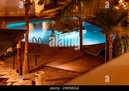 Nachtansicht auf einen beleuchteten Swimmingpool mit blauem Hintergrund, Palmen auf der Terrasse eines Resorts, von einem Balkon aus gesehen, ruhige Nacht in Baja California Stockfoto