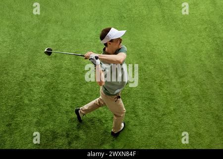 Geschickt, fokussiert auf den Golfspieler von oben am Ende des Schwungs posiert auf dem üppig grünen Golfplatz. Männliches Modell mit Blick auf die Entfernung. Stockfoto