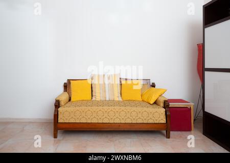 Ein klassisches Holzsofa mit gelben Kissen bringt Wärme in eine gemütliche Ecke und strahlt Vintage-Charme und Komfort aus Stockfoto