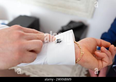 Ein Mann bereitet sich auf seine Hochzeit vor, indem er sorgfältig elegante Manschettenknöpfe an seinem Hemd befestigt, eine Geste der Liebe zum Detail Stockfoto