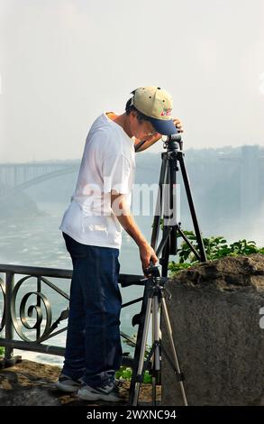 Das Stockfoto zeigt einen asiatischen Fotografen, der sein Stativ an den Niagarafällen in Kanada aufstellt. Stockfoto