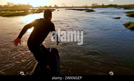 Tragflächenreiter gleitet mit seinem Brett in einem der Kanäle der Ria de Aveiro in Portugal während des Sonnenuntergangs über dem Wasser. Stockfoto