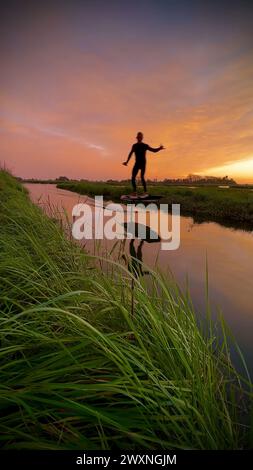 Tragflächenreiter gleitet mit seinem Brett in einem der Kanäle der Ria de Aveiro in Portugal während des Sonnenuntergangs über dem Wasser. Stockfoto