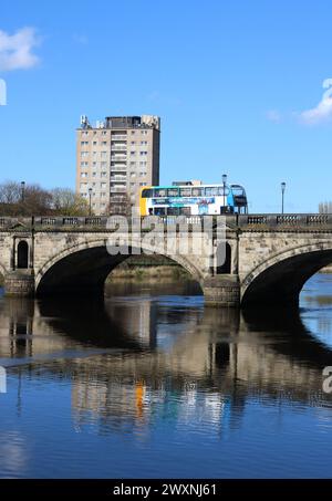Postkutsche Doppeldeckerbus überquert die historische Skerton Bridge über den Fluss Lune in Lancaster, Lancashire, England bei Flut am 30. März 2024. Stockfoto