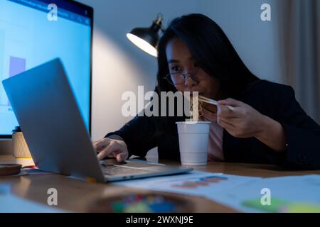 Die junge Frau arbeitete spät und isst jetzt Instant-Nudeln im Büro Stockfoto