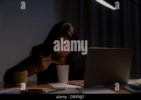 Die junge Frau arbeitete spät und isst jetzt Instant-Nudeln im Büro Stockfoto