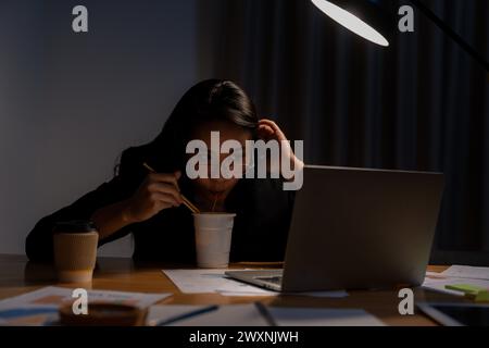 Die junge Frau arbeitete spät und isst jetzt Instant-Nudeln im Büro Stockfoto