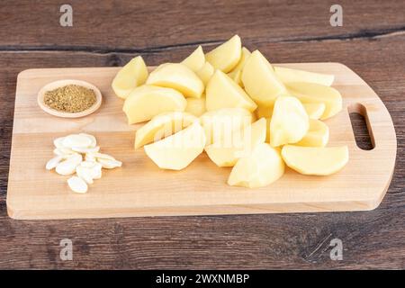 Schälen Sie geschnittene rohe Kartoffeln, Knoblauchleisten und Gewürze auf einem Schneidebrett. Kopierbereich. Stockfoto