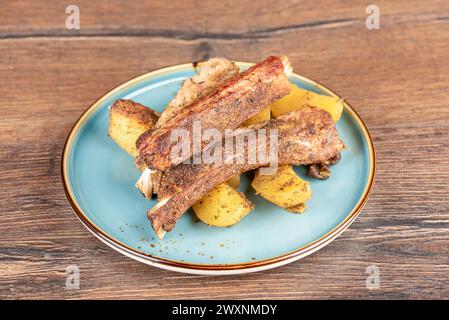 Gebackene Schweinerippchen mit Kartoffeln auf einem Teller auf einer hölzernen Arbeitsplatte. Hausmannskost. Stockfoto
