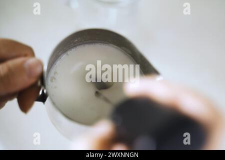 Nahaufnahme einer Person, die Latte Art kreiert, indem sie gekonnt aufgeschäumte Milch in eine Kaffeetasse gießt und dabei die Expertise der Barista in der Getränkevorbereitung zeigt Stockfoto