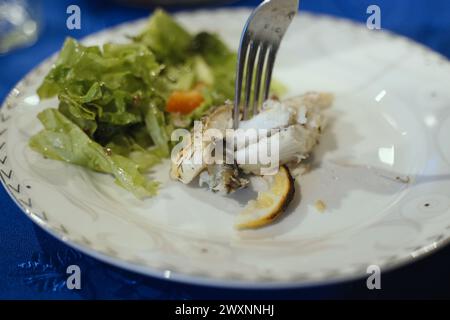 Ein weißer Teller mit einem Stück Fisch neben einem lebhaften Salat. Stockfoto