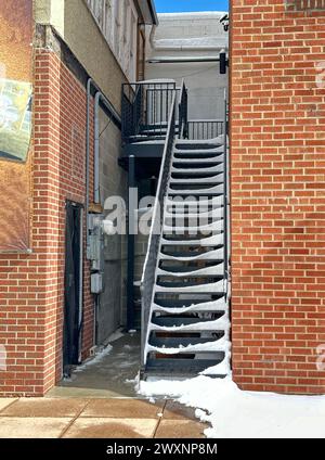 Eine Außentreppe mit Schneemuster führt zum Zimmer im Obergeschoss. Das Gebäude aus rotem Backstein zeigt einen seitlichen Eingang zur Versorgungsanlage. Das Hotel befindet sich in einem Geschäftsviertel. Stockfoto