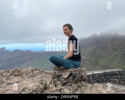 Eine junge Frau sitzt auf einem Felsen vor einer Bergkulisse Stockfoto