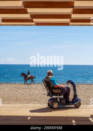 Ein älterer Mann im Rollstuhl beobachtet einen Reiter mit seinem Pferd am Strand in Mijas, Spanien. Stockfoto