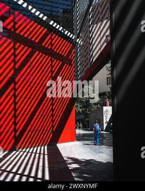 London – 18. Juli 2020 – Street Photography of man Walking next to Shadow Patterns and Red Wall, London UK Stockfoto