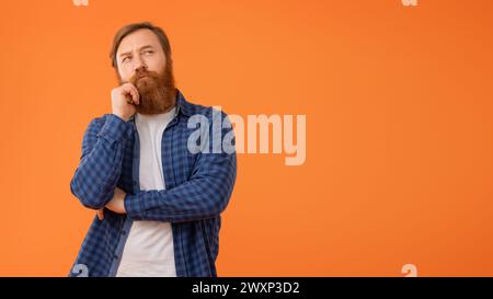 Nachdenklicher rothaariger bärtiger Geschäftsmann im beiläufigen Denken vor orangem Hintergrund Stockfoto
