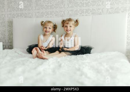 Zwei kleine weibliche Kinder sitzen auf einem kleinen Bett in einem Zimmer. Sie wirken entspannt und engagiert in Gesprächen oder Spielen. Stockfoto