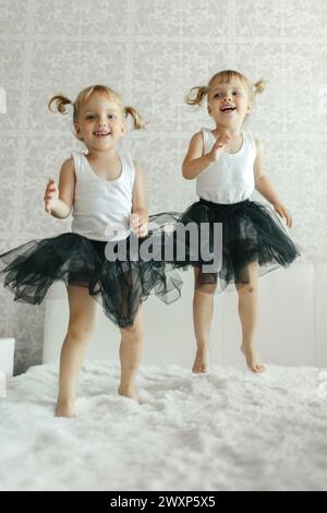 Zwei junge Mädchen springen glücklich auf ein Bett im Schlafzimmer, lachen und haben Spaß miteinander. Stockfoto