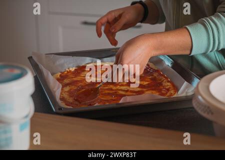 Die Frau verteilt hausgemachte Tomatensauce auf Pizzateig in einer Pfanne. Hausgemachte Pizza, die zu Hause gebacken wird Stockfoto