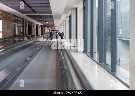 Innendurchfahrt im Flughafen Berlin-Schönefeld, sichtbare Wanderwege und lange Gassen. Einige Personen sind sichtbar, die in Richtung des Ausgangs gehen. Flughafentransfer Stockfoto