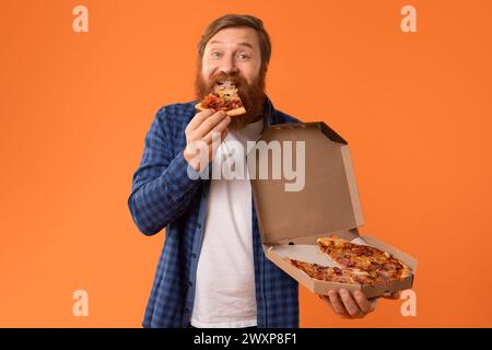 Ein fröhlicher bärtiger Kerl beißt im Studio in ein Stück Pizza Stockfoto