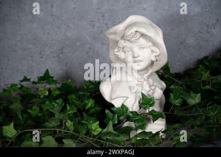 Deutschlandhohe Skulptur Kopf, Kopf aus weißem Stein geschnitzt, Mädchen mit antikem Hut. Mit grünen Blättern Stockfoto