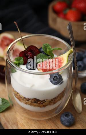 Glas mit Joghurt, Beeren, Minze und Müsli auf Holztisch, Nahaufnahme Stockfoto