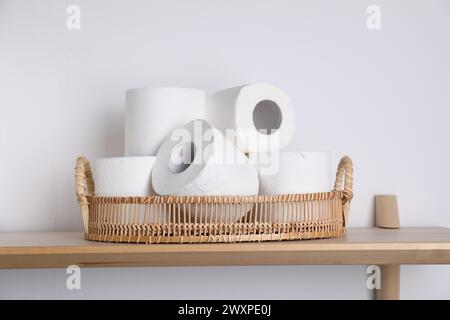 Toilettenpapierrollen im Korb auf einem Holztisch in der Nähe der weißen Wand Stockfoto