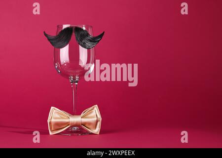 Männergesicht aus künstlichem Schnurrbart, Fliege und Weinglas auf purpurrotem Hintergrund. Leerzeichen für Text Stockfoto