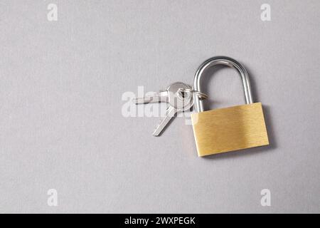 Vorhängeschloss aus Stahl mit Schlüsseln auf grauem Hintergrund, Draufsicht. Leerzeichen für Text Stockfoto