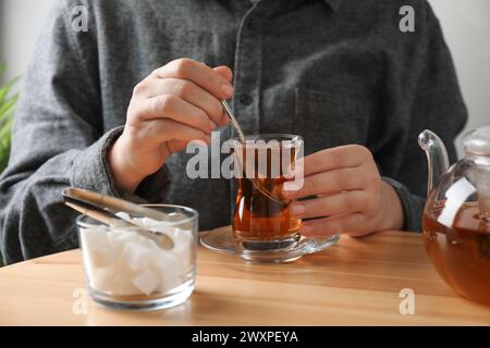 Frau rührt Zucker in Tee an Holztisch, Nahaufnahme Stockfoto