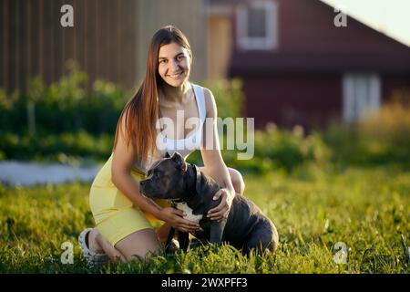Außenporträt einer jungen Europäerin mit ihrem amerikanischen Tyrannehund am Sommerabend im Dorf. Stockfoto