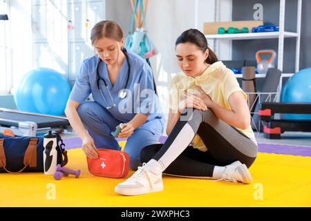 Ärztin mit Inhalator, die junge Frau erste Hilfe im Fitnessstudio gibt Stockfoto