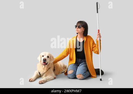 Blinde Frau mit Blindenhund auf grauem Hintergrund Stockfoto