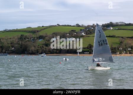 Blick auf East Portlemouth, aufgenommen von Salcombe, mit einem Segelboot im Vordergrund bei voller Segel auf ruhigem Wasser unter grauem Himmel. Stockfoto