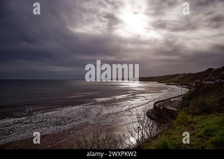 Sonnenlicht bricht durch graue Regenwolken und scheint über das Meer in einer Küstenbucht in Scarborough, North Yorkshire, England. Stockfoto
