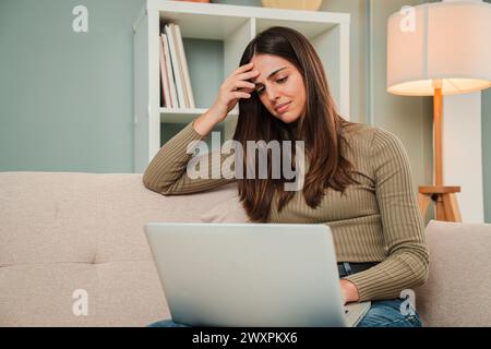 Eine Frau, die ein Finanzierungsproblem mit einem Laptop hat, der mit Schulden überfordert ist. Traurige, müde und frustrierte Frau, die mit ihrem Job unzufrieden ist und Probleme mit der Arbeit hat. Verzweifelte junge Dame mit Stress und Kopfschmerzen. Hochwertige Fotos Stockfoto