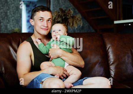 Vater mit Tochter in den Armen sitzt zu Hause auf Ledersofa. Stockfoto