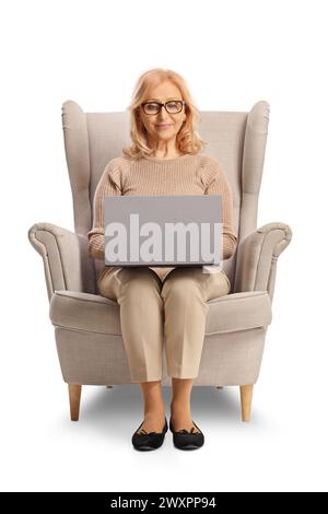 Reife Frau sitzt in einem Sessel mit einem Laptop isoliert auf weißem Hintergrund Stockfoto
