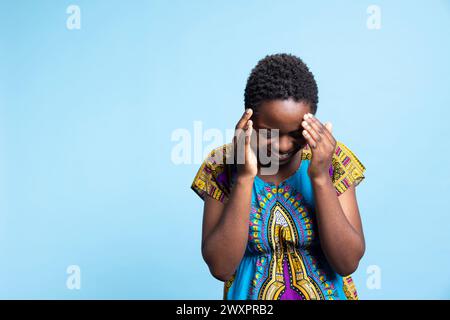 afroamerikaner lacht über einen Witz im Studio und fühlt sich glücklich und überglücklich, während sie ein traditionelles Stammeskostüm trägt. Junge Frau, die Freizeit genießt und vor der Kamera lächelt. Stockfoto