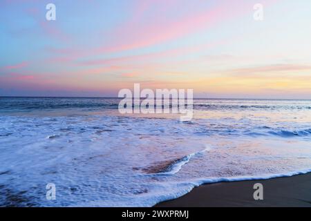Ruhige Strandszene mit den warmen Farbtönen einer untergehenden Sonne, die einen faszinierenden Glanz über die ruhige Küste zaubert Stockfoto