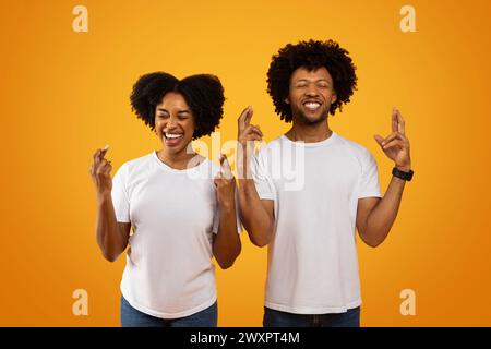 Abergläubisches afroamerikanisches Paar kreuzt die Finger auf Gelb Stockfoto