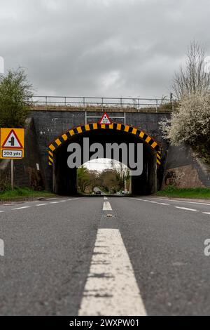 Flacher Blick auf eine ländliche Straße, die sich einem gemauerten Tunnel nähert, mit Verkehrswarnschildern Stockfoto