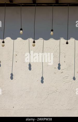 Einige hängende Glühbirnen werfen am Nachmittag ihren Schatten auf eine weiße Wand in der Kolonialstadt Villa de Leyva in Zentral-Kolumbien. Stockfoto